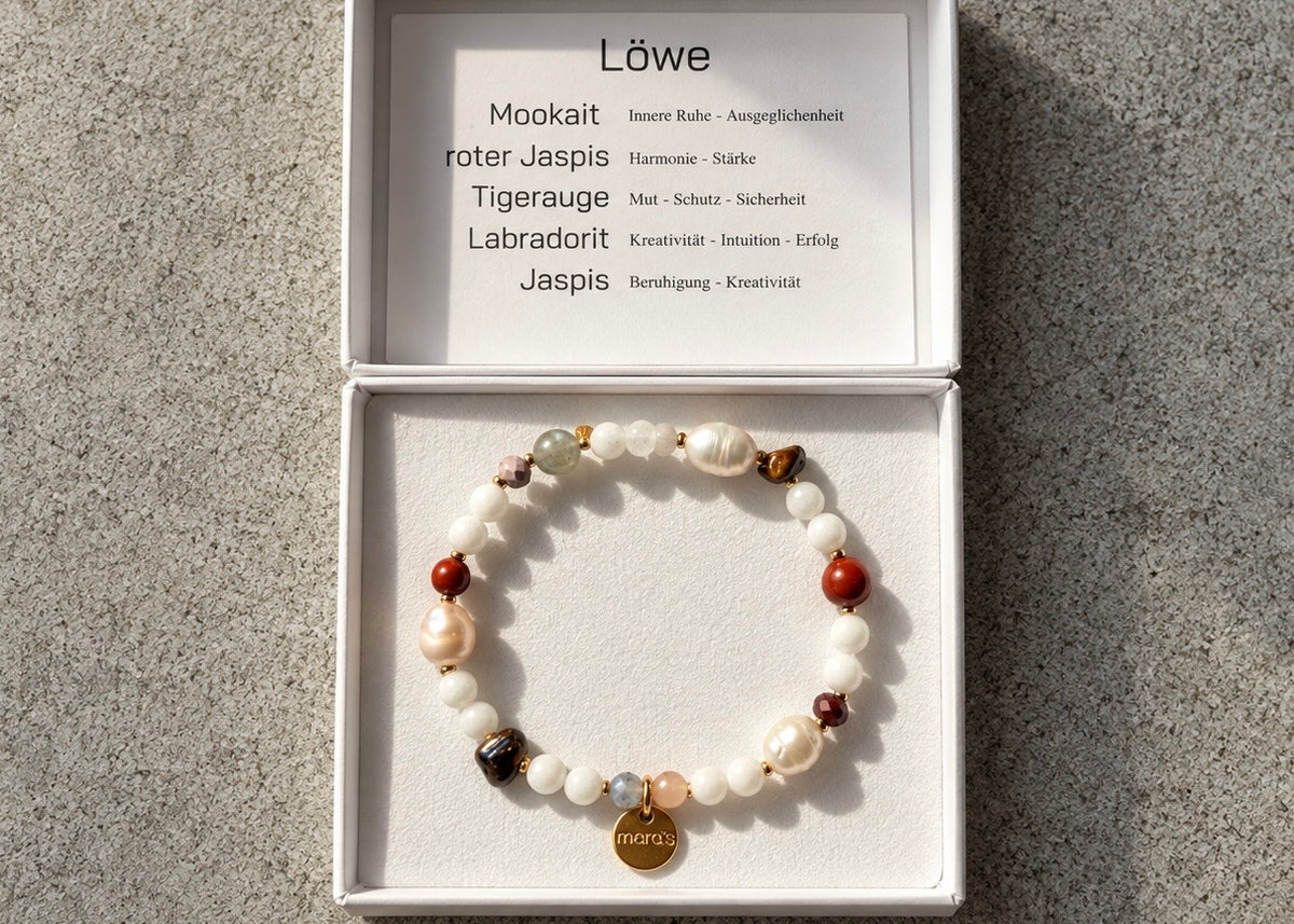 Sternzeichen-Armband Löwe mit Mookait, rotem Jaspis, Tigerauge, Labradorit und weißen Perlen in einer geöffneten weißen Schmuckschachtel.