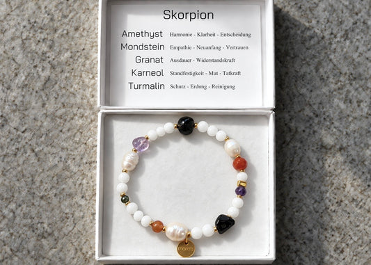 Skorpion-Sternzeichenarmband mit hellen Perlen, bunten Natursteinen und Maras-Anhänger in einer weißen Schmuckschachtel mit Edelsteinkarte.